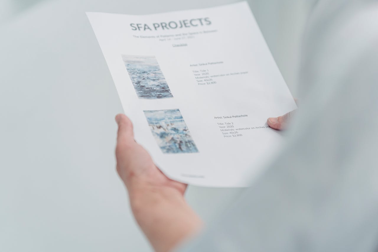 Close-up of hands holding and reading an art project document indoors.